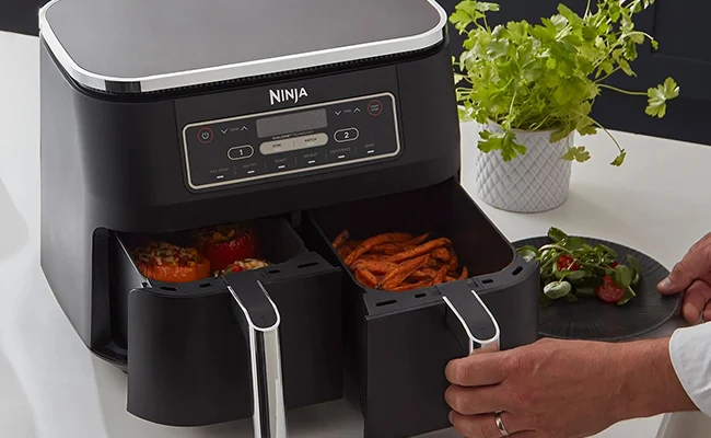 در این عکس یک سرخ کن بدون روغن ninja af300 با کشوهای باز حاوی غذای آماده شده نمایش داده شده است.