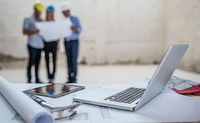 لپ تاپ و تبلت روی میزی در جلوی تعدادی مهندس